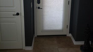 A closed white door with a keyhole and a handle, a white-framed window with blinds, and a dark wall. - Cave Creek Guest Suite (Cave Creek)