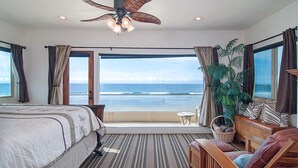 A hotel room with a bed, a seating area, a ceiling fan, and a view of the ocean.