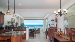 A spacious kitchen with a large island, a dining area with wooden furniture, and a view of the ocean.