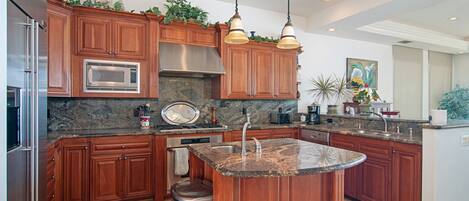 A modern kitchen with wooden cabinets, granite countertops, stainless steel appliances, and pendant lighting.