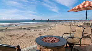 A beachside patio with a fire pit, outdoor seating, and a view of the ocean and pier.