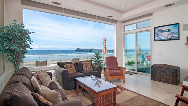 A spacious living room with a large window overlooking the beach, a cozy seating area, and a view of the ocean.
