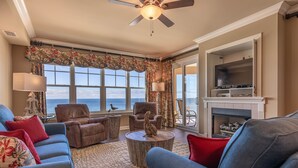 A living room with a view of the ocean, a fireplace, and a ceiling fan. - 4 BR En Soleil Directly on Gulf, 14th floor unit with the best views!! (Panama City Beach)
