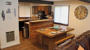 Une cuisine moderne avec des meubles en bois, un îlot central et un coin repas agrémenté d’une horloge au mur.
