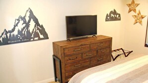 Une chambre avec une commode en bois, un téléviseur à écran plat et des autocollants muraux sur le thème de la montagne.
