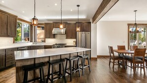 Una cocina moderna con una isla grande, taburetes de bar y una zona de comedor con sillas de madera.