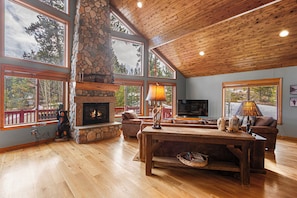 Un salón amplio con chimenea de piedra, ventanas grandes y techo de madera.