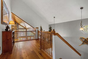 Uma escada de madeira com corrimão, uma luminária e vista para o exterior.