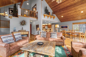 A spacious living area with a high ceiling, wooden beams, a fireplace, and a dining area with wooden furniture.