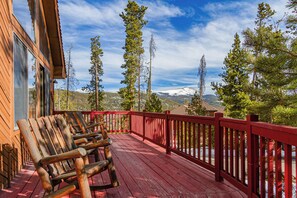 Um deck de madeira com guarda-corpos vermelhos e vista para montanhas cobertas de neve.