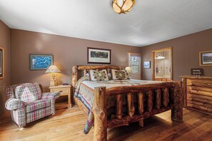 Ein Schlafzimmer mit einem Bettgestell aus Holz, einem Karosessel, einem Nachttisch und einer Kommode.