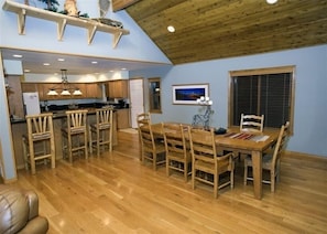 Una cocina amplia con armarios de madera, un comedor con mesa y sillas de madera, y un techo alto con vigas a la vista.
