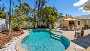 A backyard with a swimming pool, patio furniture, and palm trees. - Willow Cottage: Steps to the beach, heated pool, perfect location! (Anna Maria)