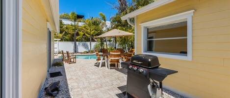 Un patio trasero con una parrilla, asientos exteriores y una piscina.