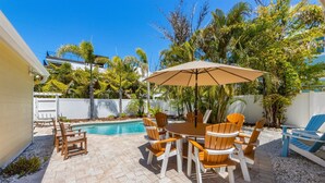 A patio with a pool, surrounded by palm trees and a white fence. - Willow Cottage: Steps to the beach, heated pool, perfect location! (Anna Maria)