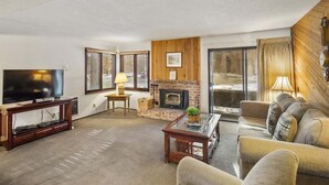 Una sala de estar con televisión, chimenea, sofá y un ventanal grande.