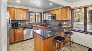 Una cocina moderna con armarios de madera, un refrigerador de acero inoxidable, un microondas y un lavavajillas. Hay dos taburetes de bar en la isla.