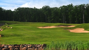 A golf course with sand bunkers, a stone wall, and a forest in the background.