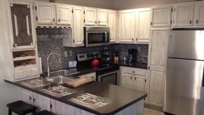 A modern kitchen with white cabinets, a central island with stools, stainless steel appliances, and a tiled backsplash.
