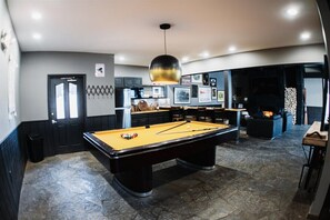 A pool table in a room with a stone floor, a black door, and a fireplace.