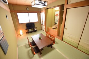 Et traditionelt japansk rum med tatamigulv, et lavt bord med hynder, et fjernsyn og en skydedør med dekorativt panel.