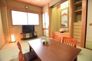 A traditional Japanese-style room with tatami flooring, a low table with chairs, a television, and a painting of Mount Fuji. - AIKAMU INN House (Osaka)