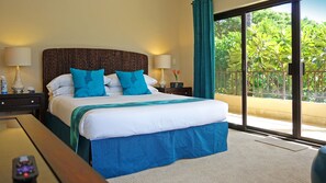 Une chambre d’hôtel avec un grand lit, deux tables de chevet, une petite table et une vue sur la verdure grâce à une porte-fenêtre coulissante.
