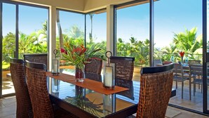 Un comedor con una mesa de vidrio, sillas de mimbre y vistas a palmeras a través de amplios ventanales.
