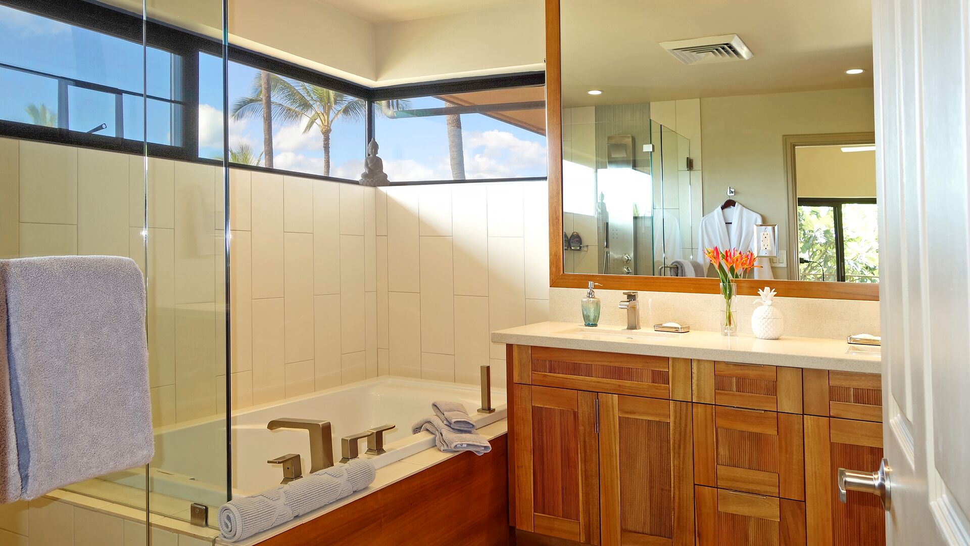 A modern bathroom with a glass shower enclosure, a bathtub, wooden cabinetry, and a large mirror reflecting a robe and a window view.