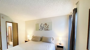 Een slaapkamer met een bed, twee nachtkastjes met lampen, een deur en een muur met een bladmotief.