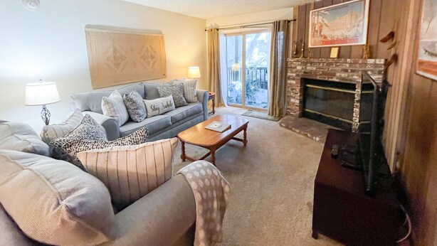 Een woonkamer met een bank, fauteuils, een salontafel, een open haard en een groot raam met gordijnen.