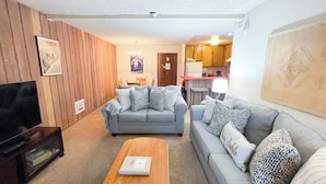 Een woonkamer met een grijze bank, een houten salontafel en een televisie op een standaard.