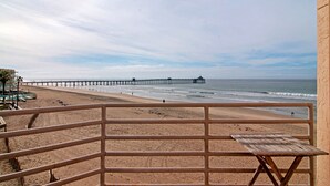 A beach view with a wooden pier extending into the ocean, a sandy beach, and a railing in the foreground. - San Diego County Oceanfront 3 bedroom-heated pool/jacuzzi. Complex on the sand (Imperial Beach)