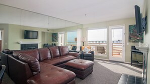 A living room with a brown leather sectional sofa, a flat-screen TV mounted on the wall, and a large mirror reflecting the room. - San Diego County Oceanfront 3 bedroom-heated pool/jacuzzi. Complex on the sand (Imperial Beach)