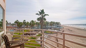 A balcony with wicker chairs overlooking a beach with palm trees and a pier. - San Diego County Oceanfront 3 bedroom-heated pool/jacuzzi. Complex on the sand (Imperial Beach)