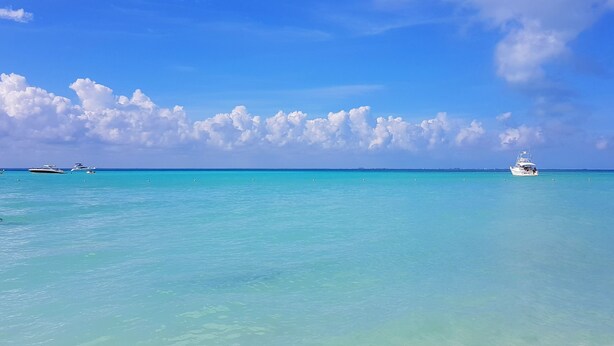 Mar azul cristalina con un barco a lo lejos y un cielo despejado.