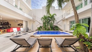 Un área de piscina en la azotea con sillones, un sofá rojo y una escalera que conduce a un nivel superior.