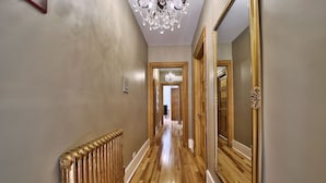 Un pasillo con piso de madera, un radiador, un candelabro y un espejo grande.