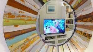 A circular mirror with a sunburst pattern reflecting a room with a television, bookshelf, and framed picture. - Sweet 1 BDRM Cottage, FAST WIFI, near ocean, W&D, Full kitchen and bath, BBQ! (Santa Cruz)