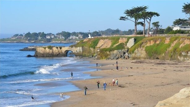 A beach with people walking, a rocky cliff, and a white building in the background. - Sweet 1 BDRM Cottage, FAST WIFI, near ocean, W&D, Full kitchen and bath, BBQ! (Santa Cruz)