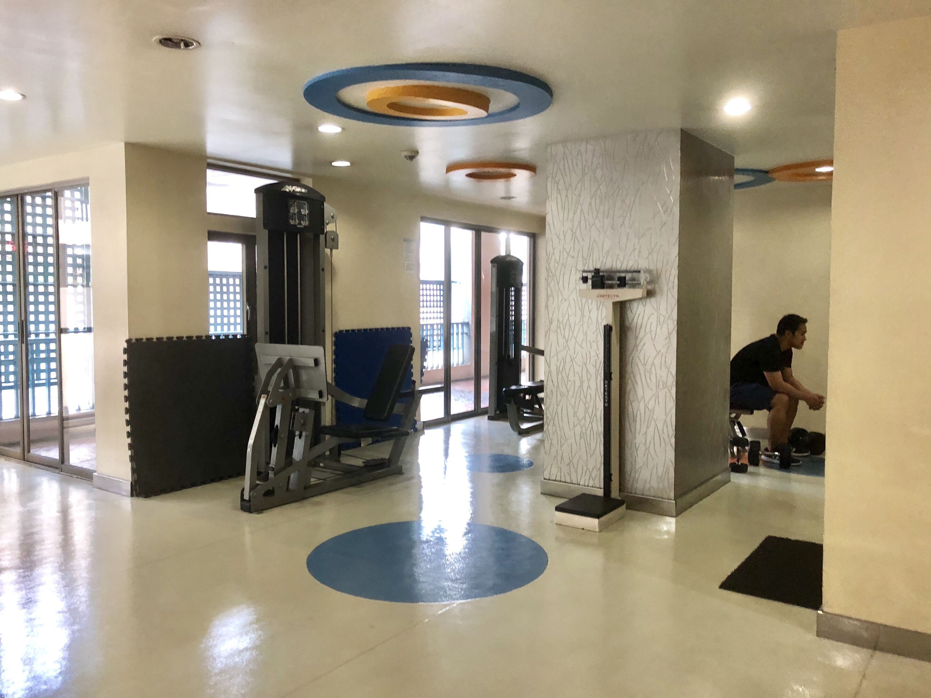A gym with exercise equipment, a blue mat, and a person using a machine.