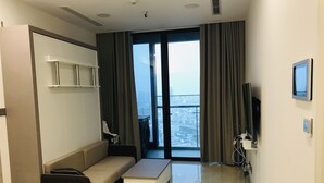 Una habitación de hotel moderna con sofá, una mesa de centro, televisión y un amplio ventanal con vistas a la ciudad.