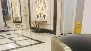 Un vestíbulo de hotel con suelo de mármol, una mesa de recepción y una alfombra estampada.