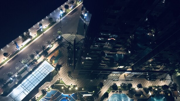 Vista aérea de un moderno complejo hotelero con múltiples piscinas, jardines ajardinados y una calle bien iluminada.
