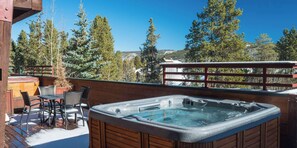 A hot tub on a wooden deck with a view of trees and a mountain in the background.