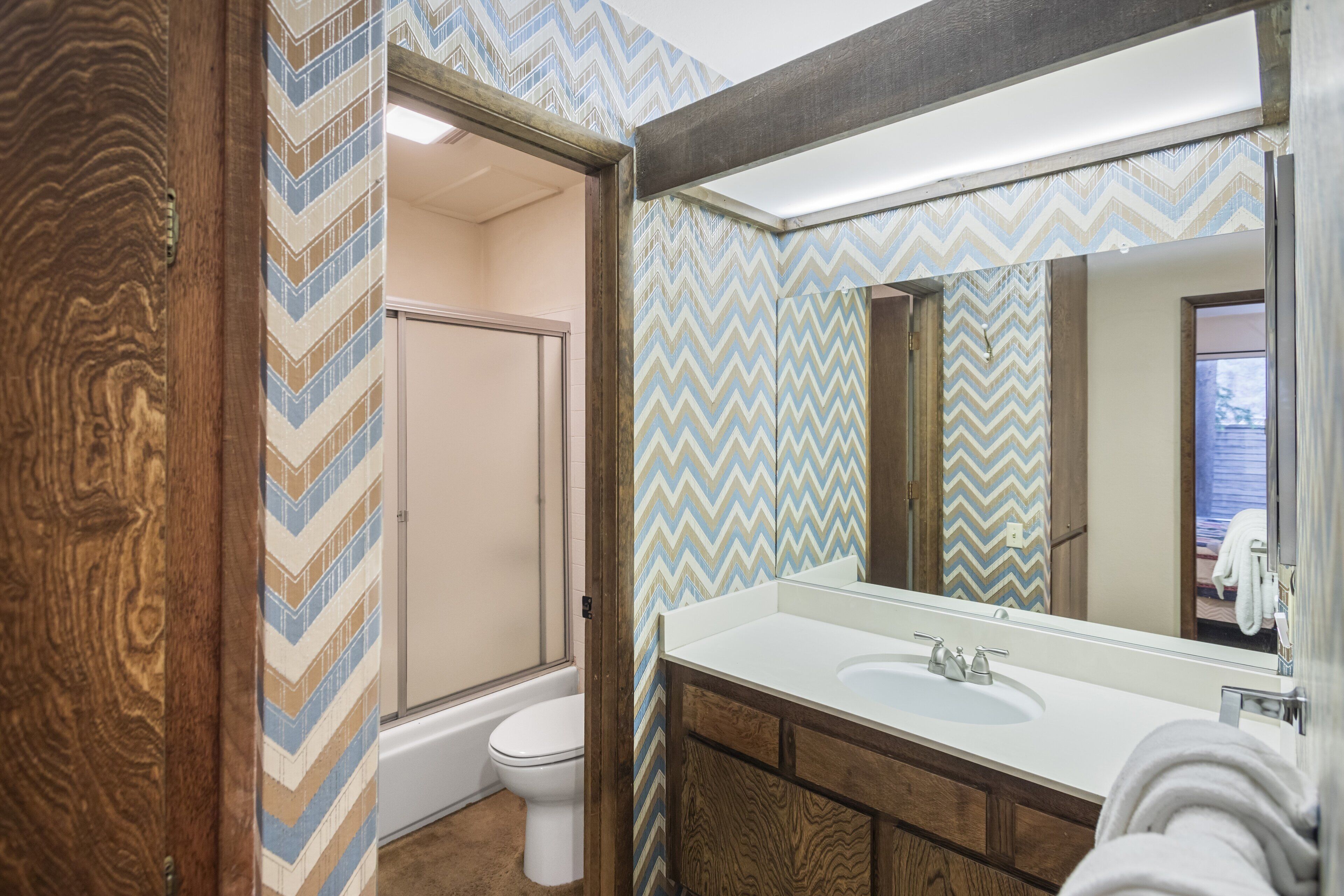 A bathroom with a wooden vanity, a large mirror, and a shower area.