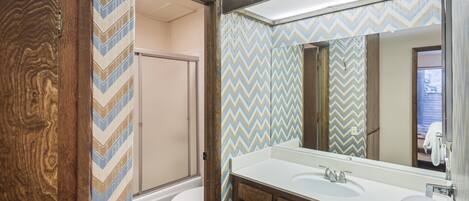 A bathroom with a wooden vanity, a large mirror, and a shower area.