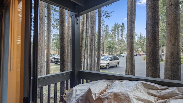 A view from a window with a metal railing, overlooking a parking area with several cars and tall trees in the background. - Sunshine Village 167 (Mammoth Lakes)