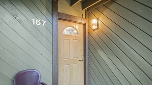 A wooden door with the number 167, a porch chair, and a light fixture on the wall. - Sunshine Village 167 (Mammoth Lakes)