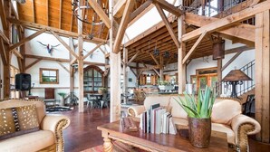 A spacious interior with high ceilings and exposed wooden beams, featuring a central seating area with a coffee table, books, and a potted plant. - Designer Barnhouse located just 8 minutes from Main St on Private Gated Ranch (Fredericksburg)